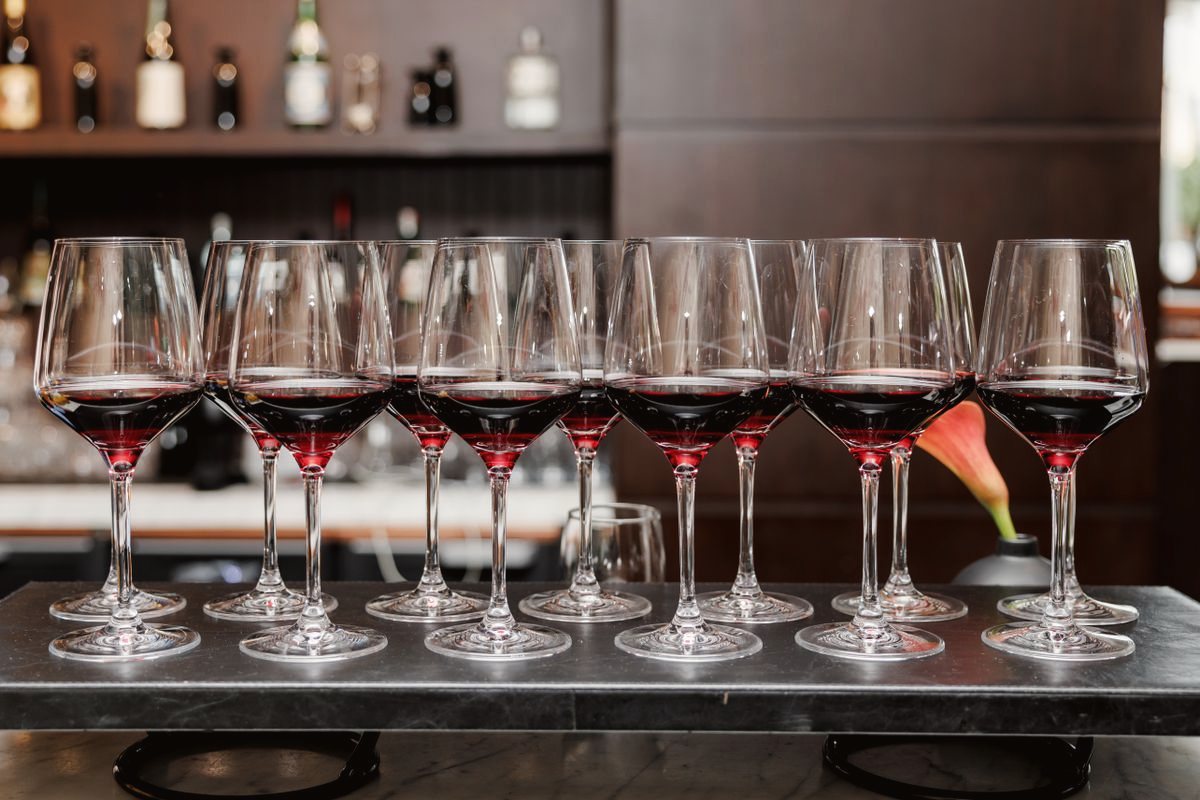 A row of glasses of red wine lined up on a dark bar