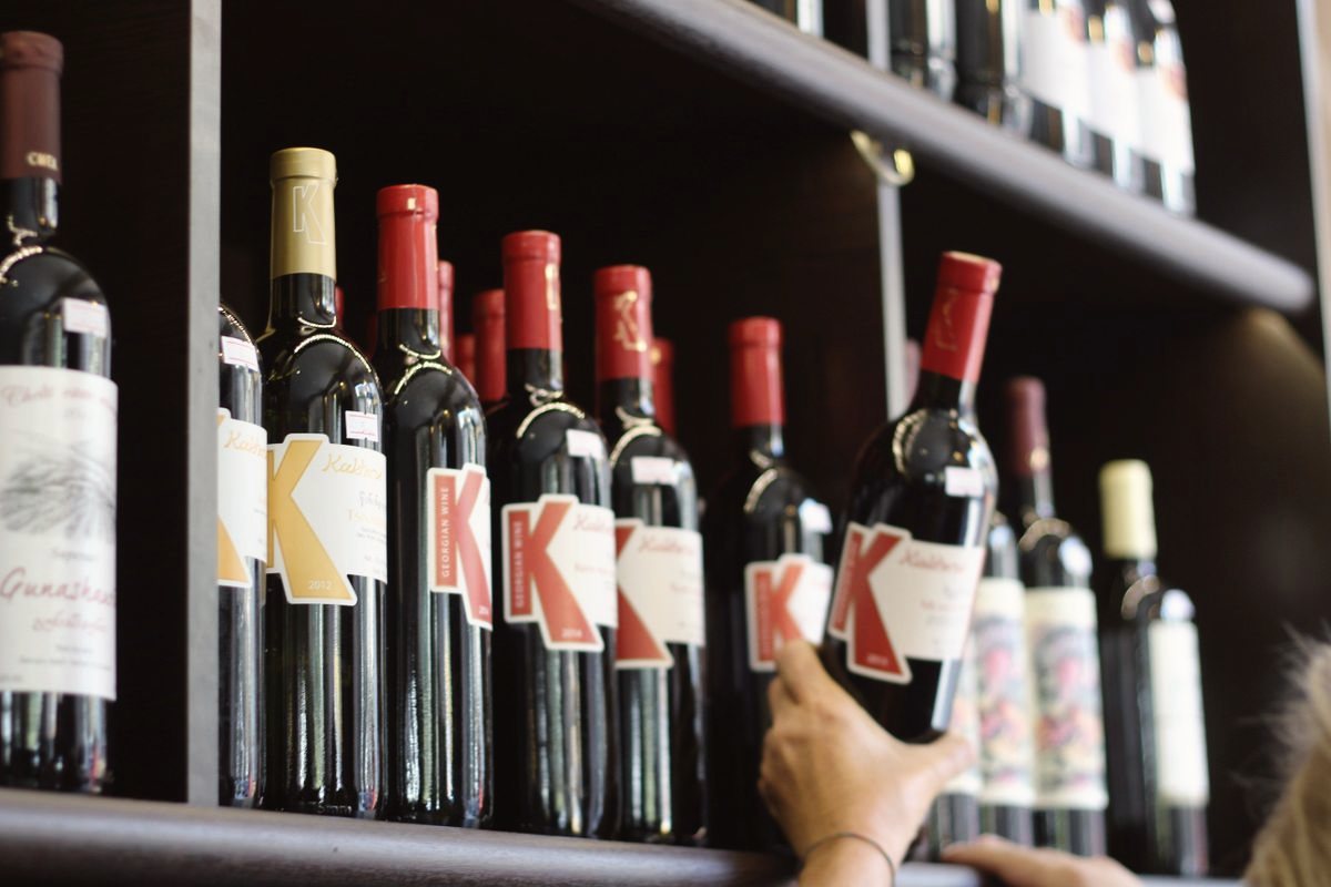 A hand pulling a bottle of red wine off a dark wooden shelf