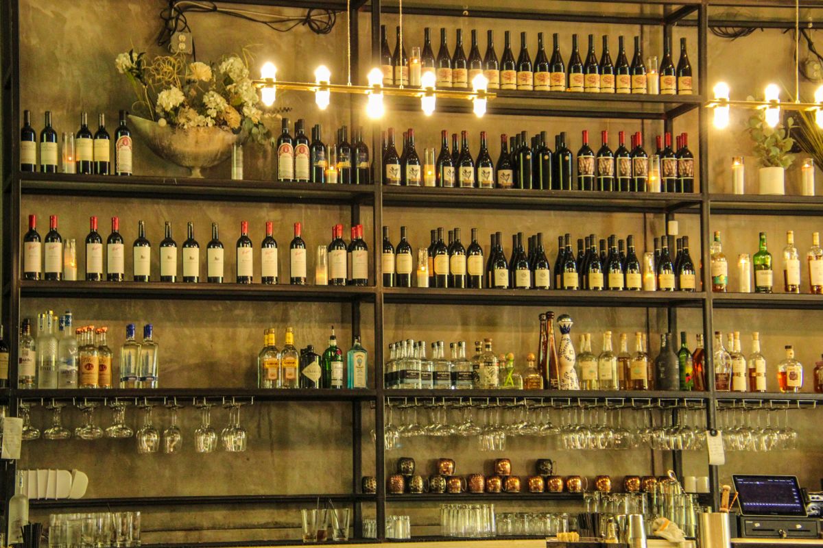 A wine bar wall of bottles on dark metal shelves under warm hanging bulbs