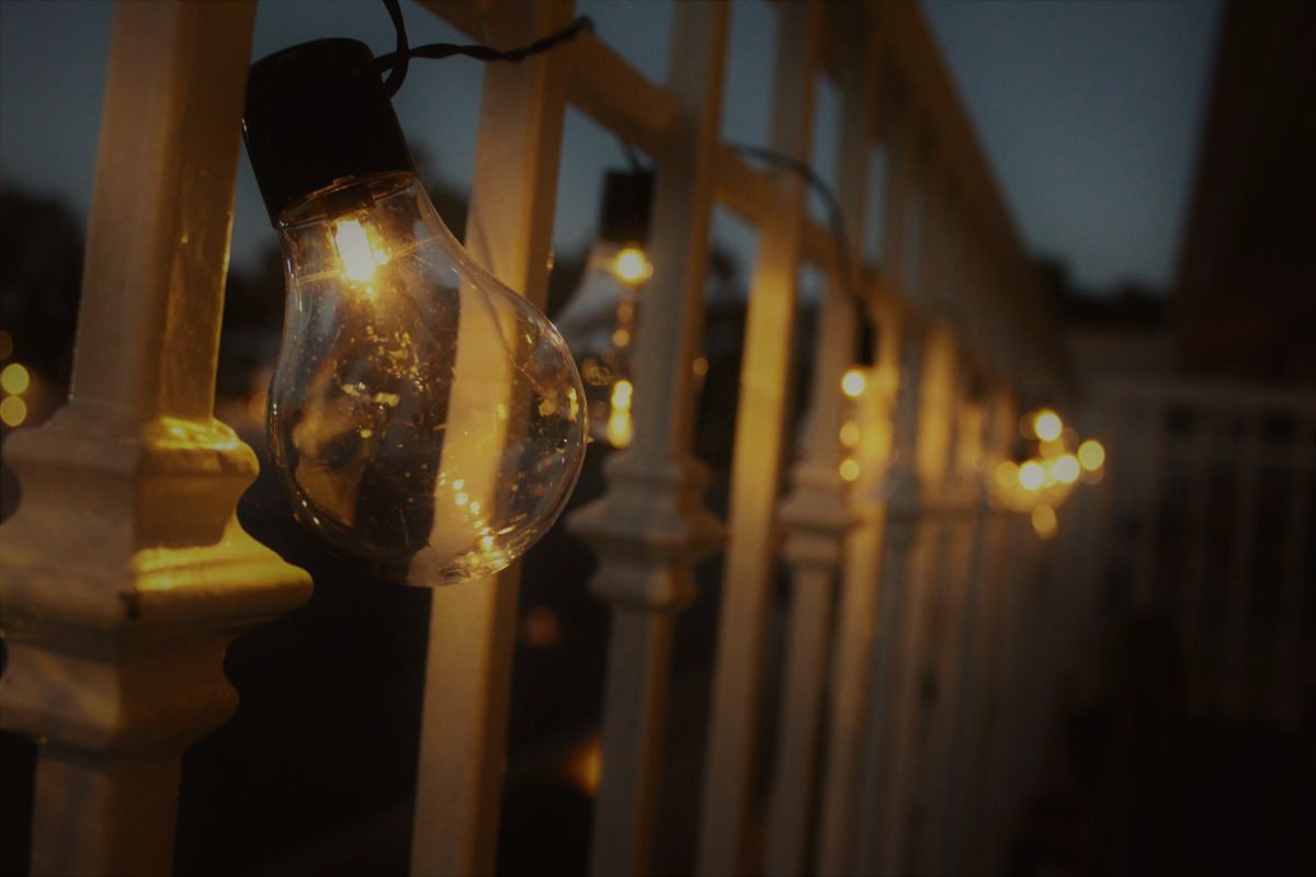 An Edison bulb glowing on a white railing at dusk