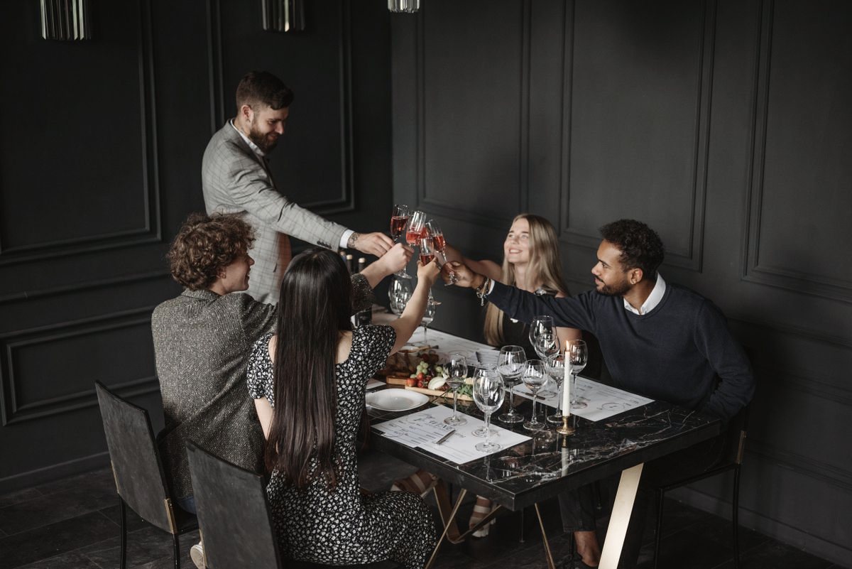 Five people raising glasses for a toast around a table in a dark-panelled room